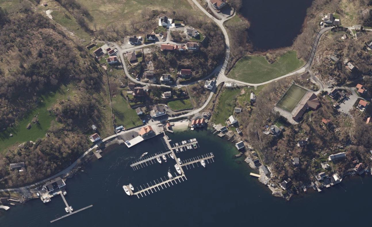 Flyfoto av Skardtveitvågen, med småbåthavn, sandstrand, landhandel, hytter og boliger.