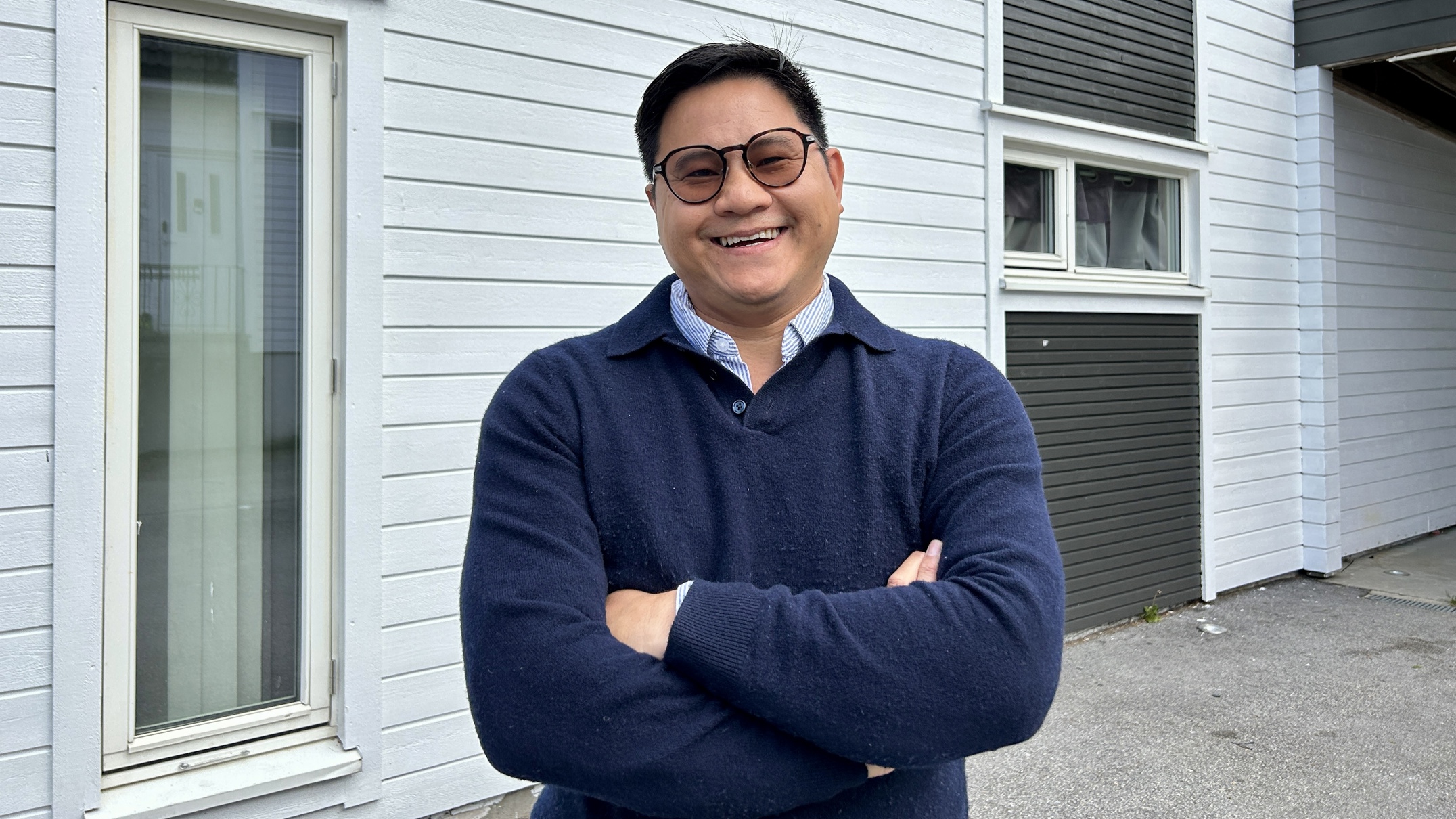 Phuong Pham ble den første som vant hovedpremien i Stavangeravtalens månedlige trekning. En mann med blå genser med blå skjorte under står foran et hvit hus og smiler med armene i kryss. Han har mørke briller og smiler bredt.