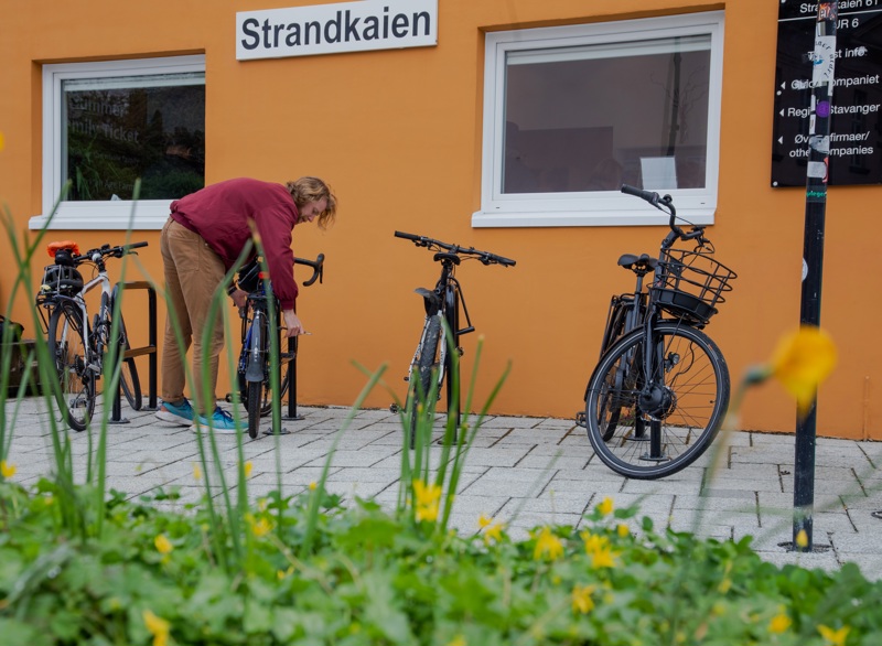 Mann låser sykkelen sin til sykkelparkering ved Strandkaien